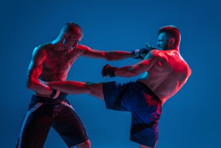 Tensioned. MMA. Two professional fighters punching or boxing isolated on blue studio background in neon. Fit muscular caucasian athletes or boxers fighting. Sport, competition and human emotions, ad.